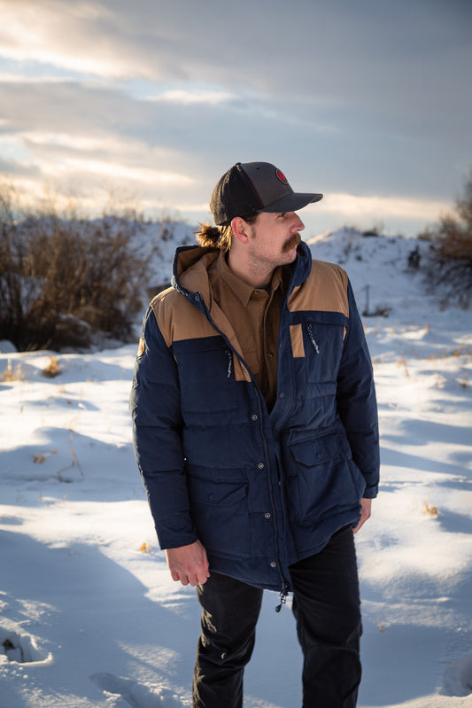 A man wears Pine Peak Down Parka standing in the snow. 